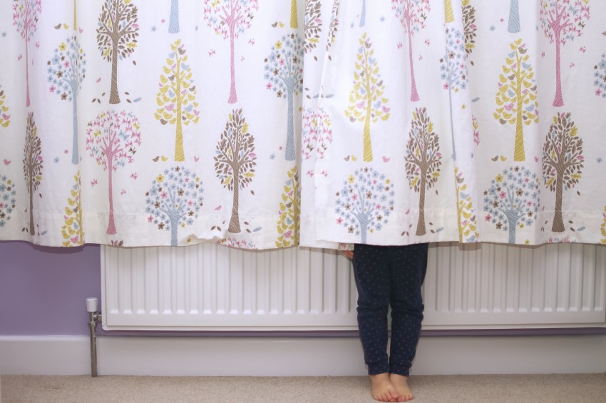 A young girl hiding behind curtains so that you can only see her legs